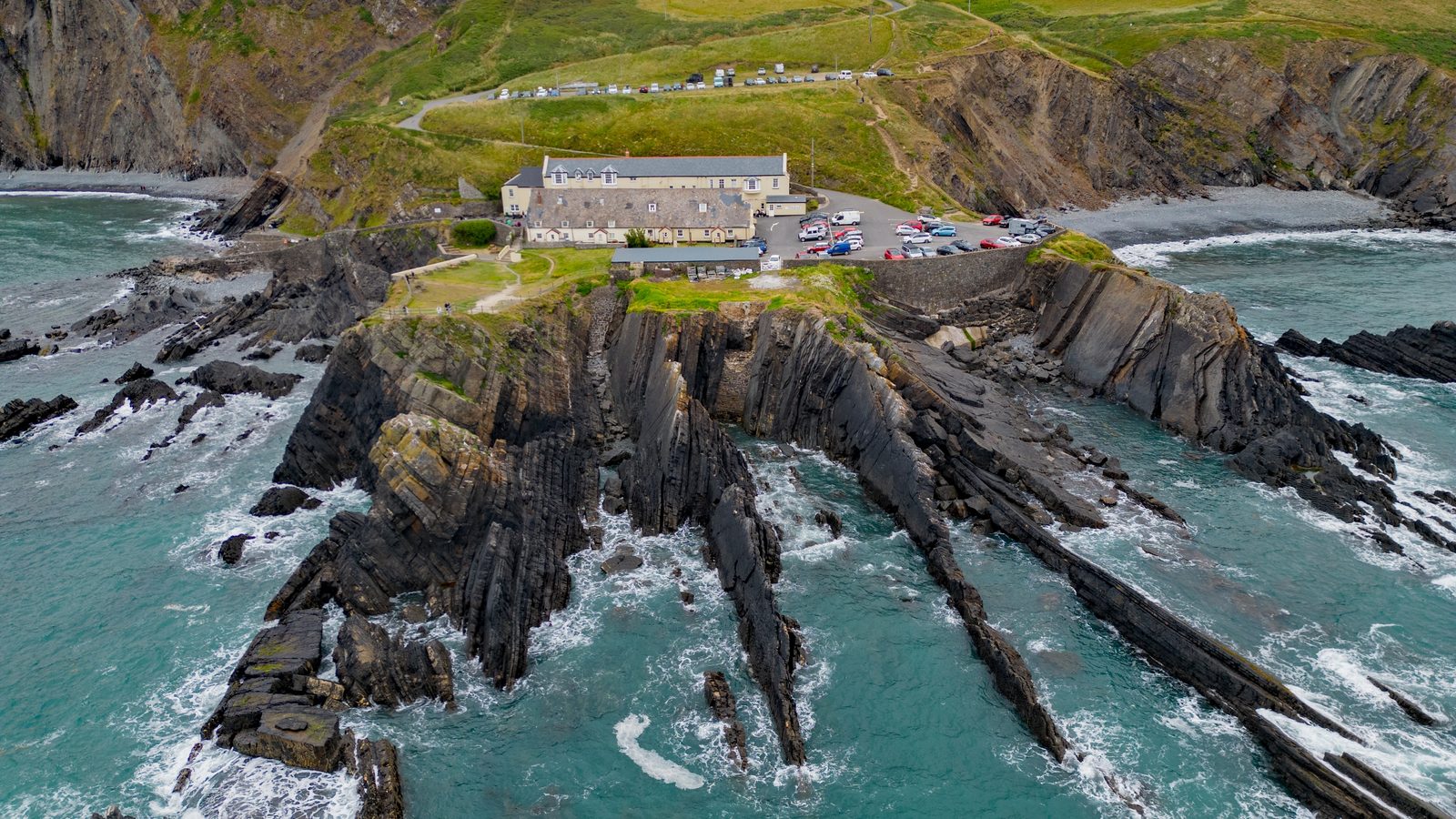 Aerial view of the tilted rock strata and hotel at Hartland Quay on the North Devon coast, with cliffs beyond