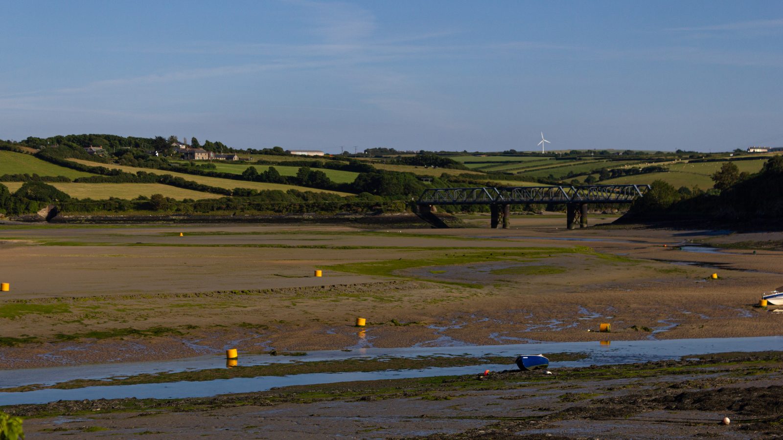 A tidal estuary at low water with moored boats and an iron railway bridge, at the Padstow end of the Port Isaac to Padstow stage